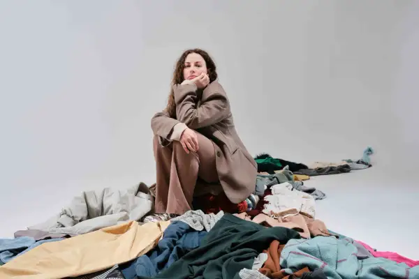 Donna pensierosa seduta su un cumulo di vestiti, simbolo del consumismo del brand fast fashion.