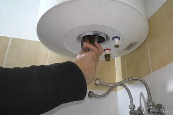Mano che estrae la resistenza scaldabagno elettrico. Riparazione fai da te.