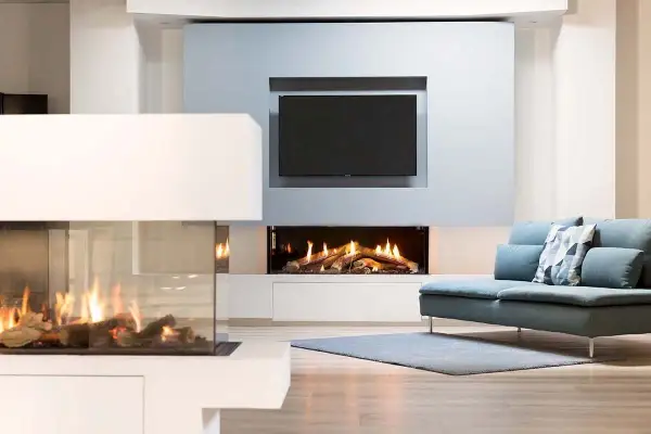 Modern living room with two elegant caminetti senza canna fumaria, one with glass enclosure, and a TV above a fireplace.