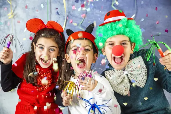 Bambini festosi con vestiti di carnevale creativi, realizzati con materiale riciclato, lanciano coriandoli.