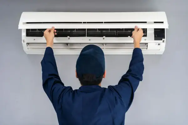 Tecnico apre il pannello di un condizionatore split per manutenzione. Il riscaldamento con split è efficiente.