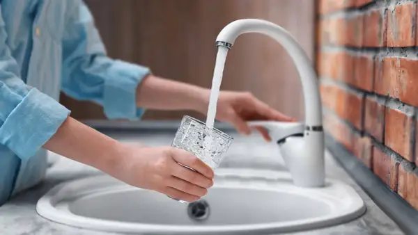 Mani che riempiono un bicchiere d'acqua dal rubinetto. L'acqua sanitaria cos'è? È l'acqua potabile che arriva nelle nostre case.